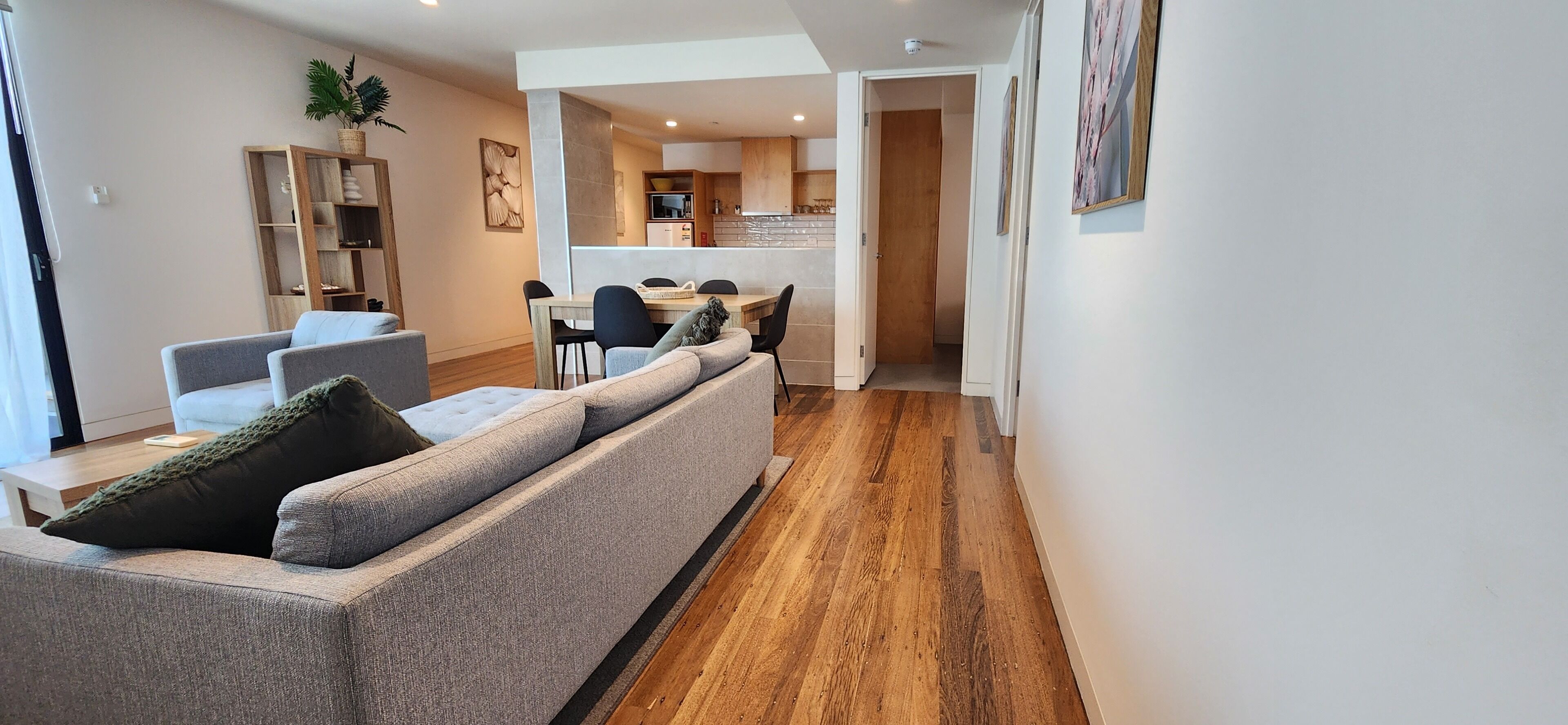 Una sala de estar moderna con un sofá gris, una mesa de comedor de madera y una cocina al fondo.