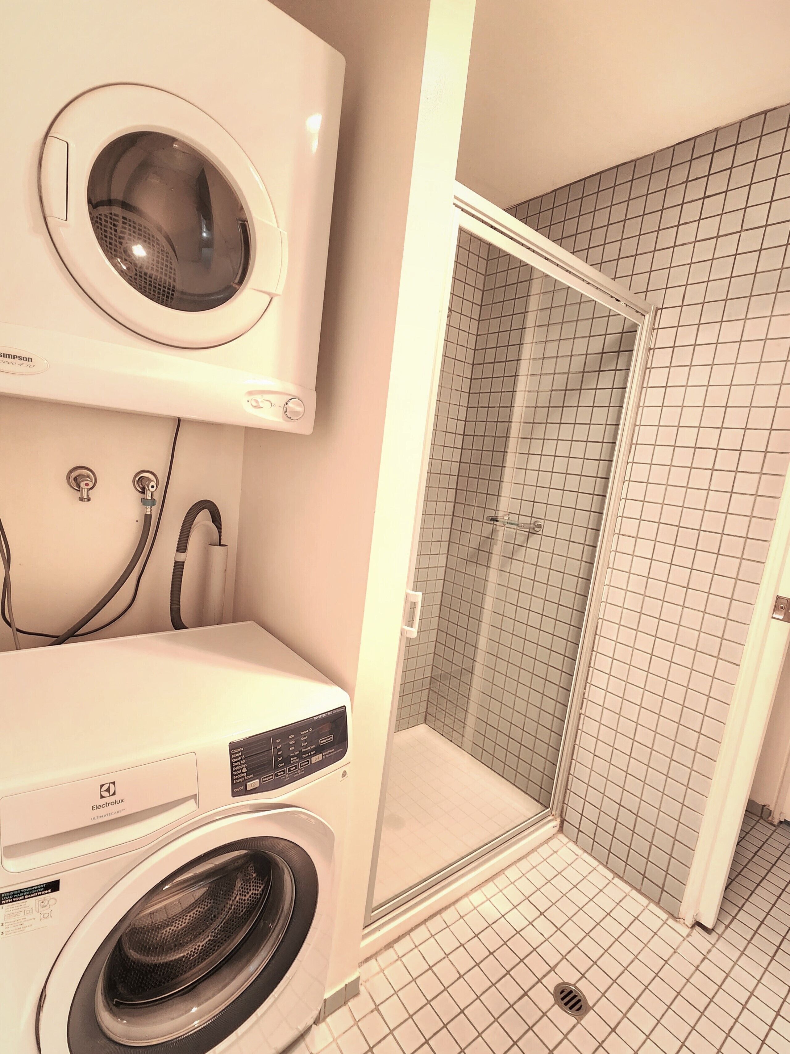 A laundry room with a front-loading washer and dryer, a tiled shower area, and a visible plumbing setup.