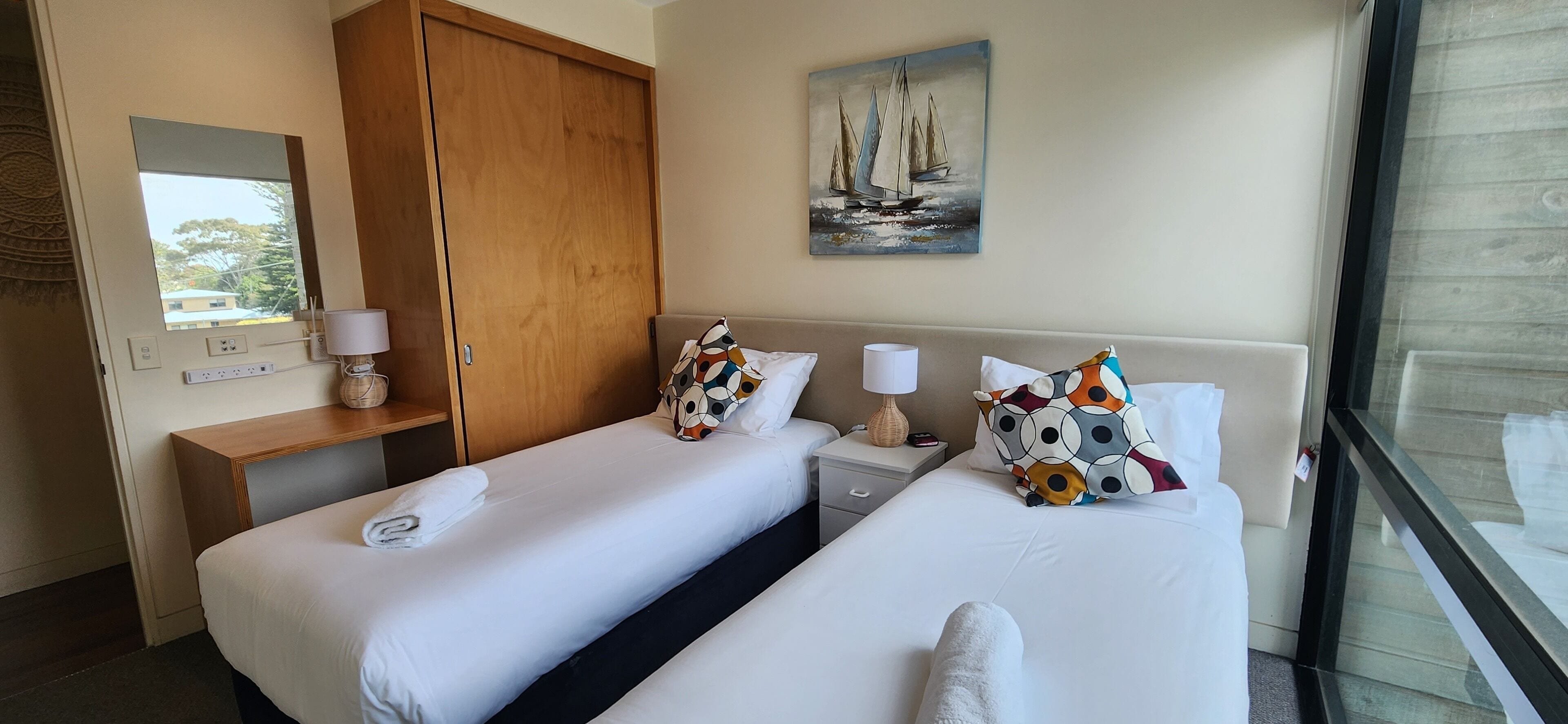 Habitación de hotel con dos camas, un armario de madera, un cuadro de veleros y ventana con vistas.