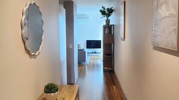 A hallway with wooden flooring, a small table with a plant, a mirror, and a framed picture on the walls.