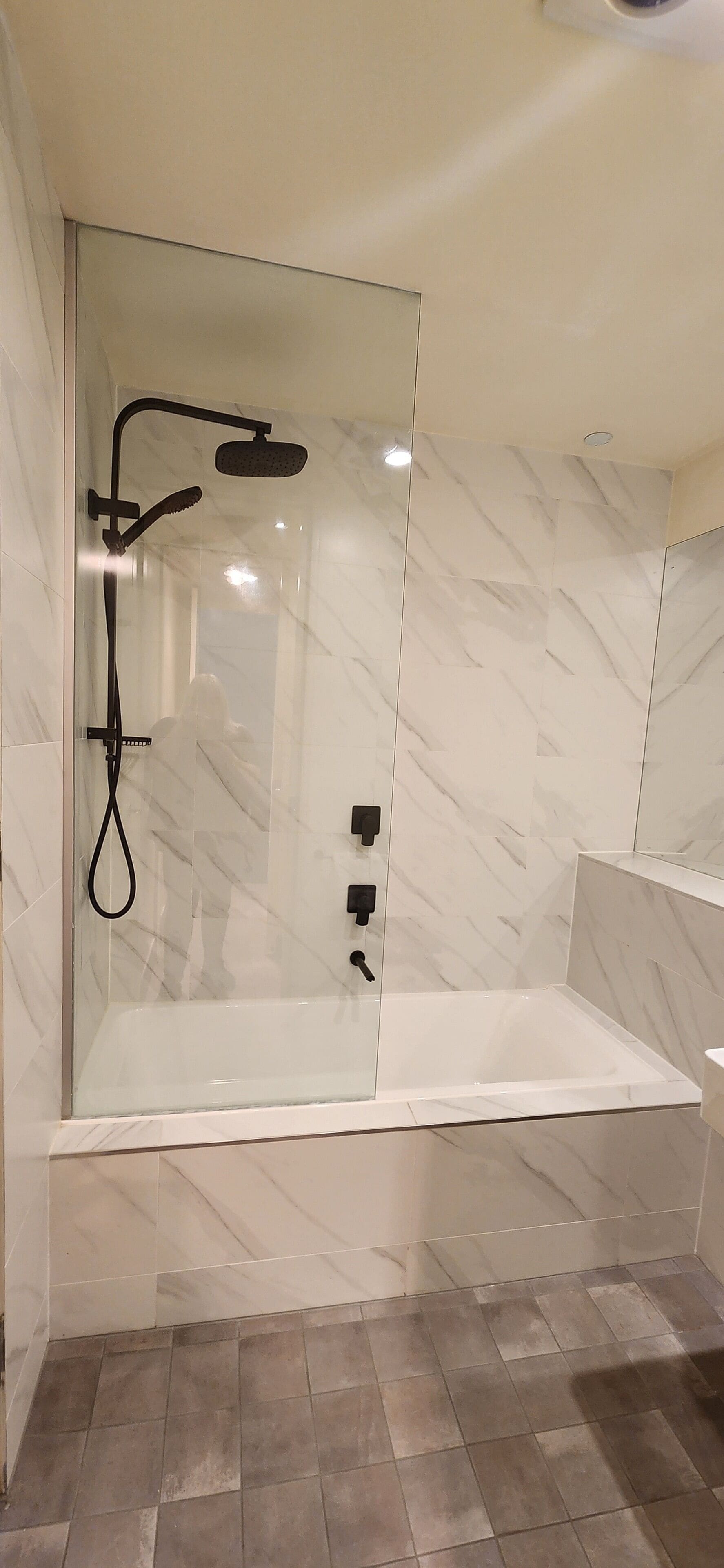 Een douche met glazen wanden, een handdouche en een douchekoof, een badkuip met glazen wanden, en een wand met een marmerlook.