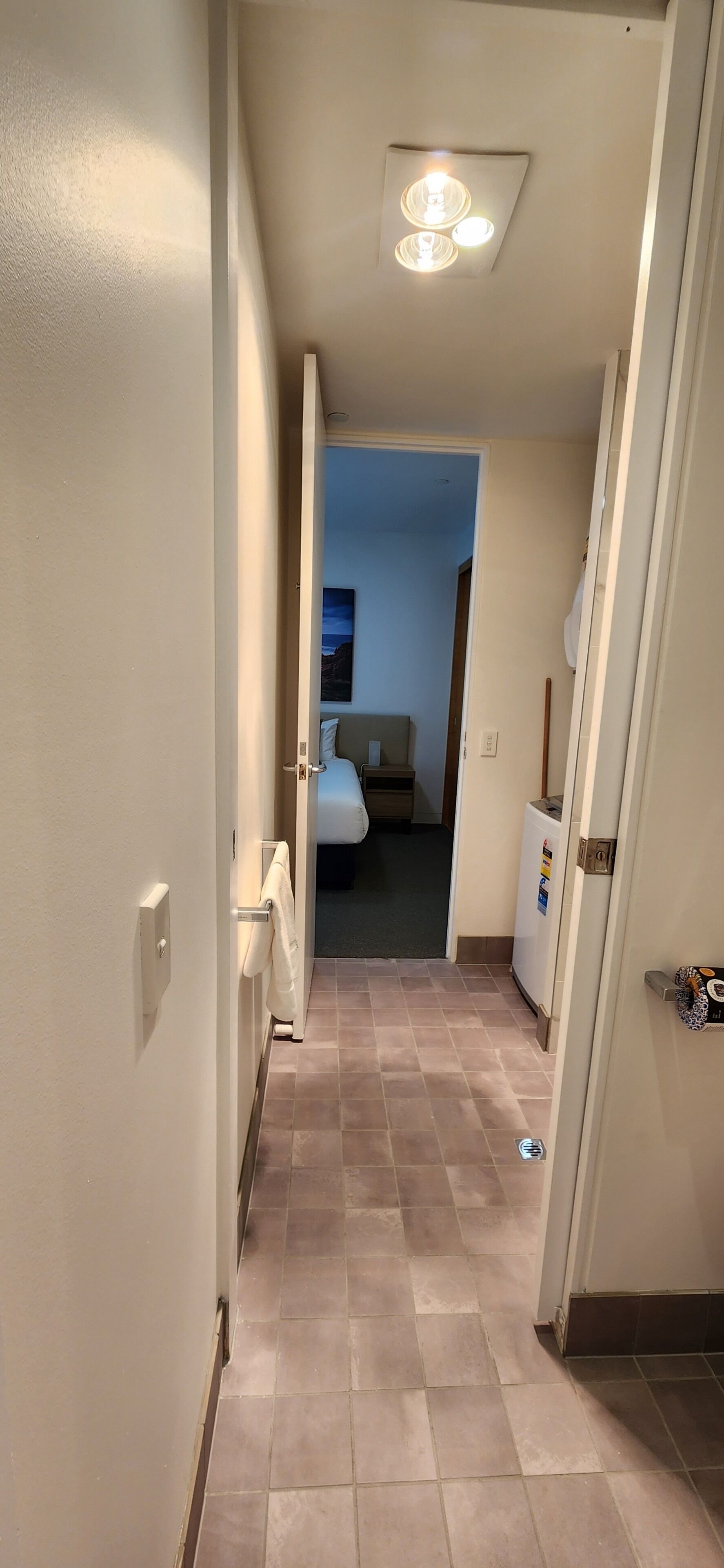 Een hotelgang met een bed, een kleine koelkast en een plafondlamp.
