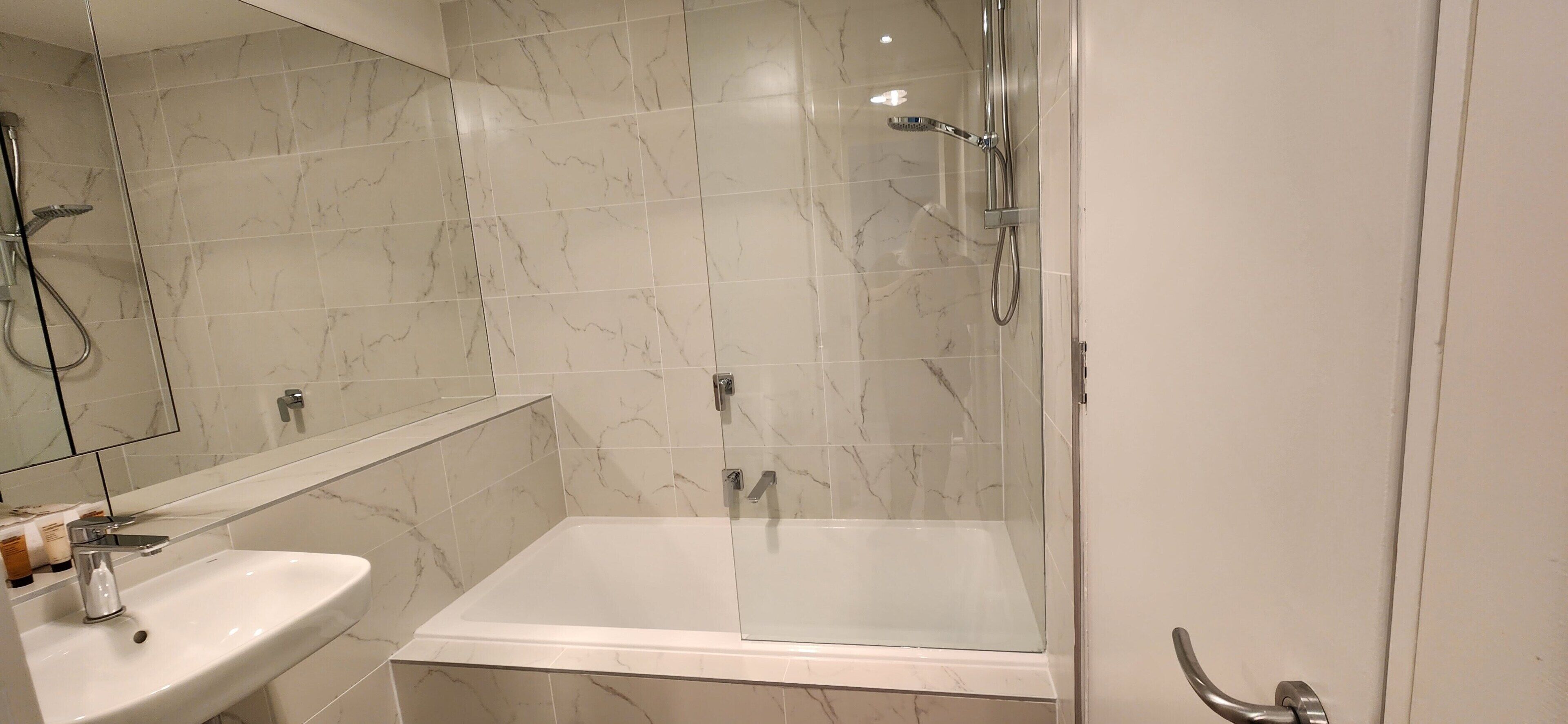 Un baño moderno con ducha de vidrio, lavamanos blanco y paredes cubiertas de mármol.