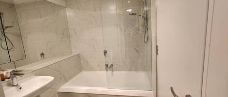 A modern bathroom with a glass-enclosed shower, a white sink, and marble-tiled walls.