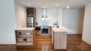 A modern kitchen with wooden cabinets, a built-in oven, and a white countertop. - Phillip Island Apartments (Cowes)