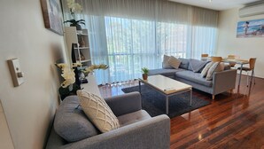 A modern living room with a grey sofa, a coffee table, and a dining area with chairs. - Phillip Island Apartments (Cowes)