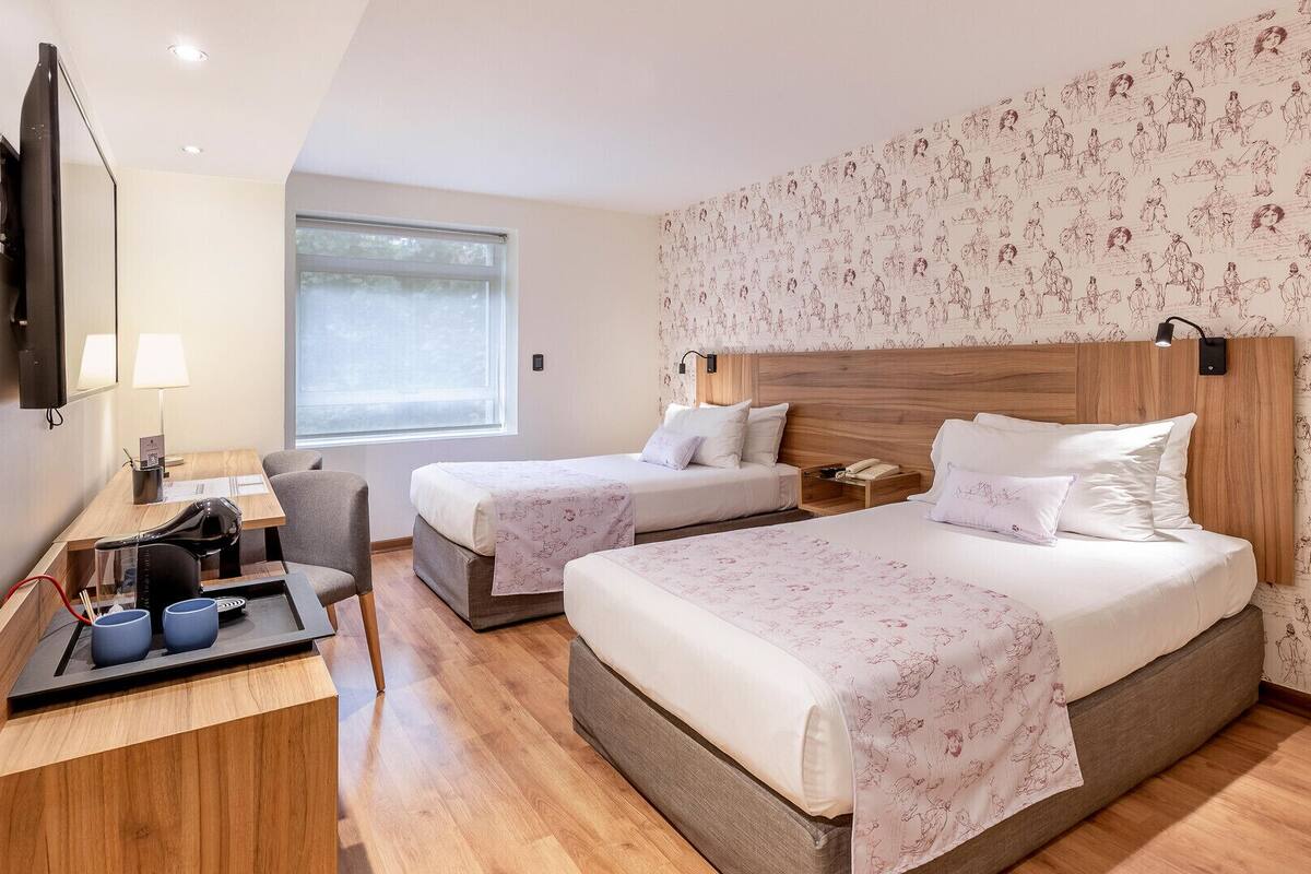 A hotel room with two beds, a desk, a chair, a TV, and a large window.