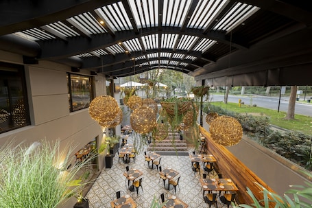 A modern indoor dining area with tables and chairs, a curved ceiling with lighting, and a view of the outdoors.