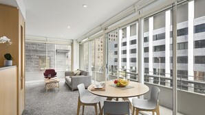 Una habitación de hotel moderna con un ventanal grande, una mesa redonda con sillas, un sofá y un pequeño escritorio con una planta en maceta.