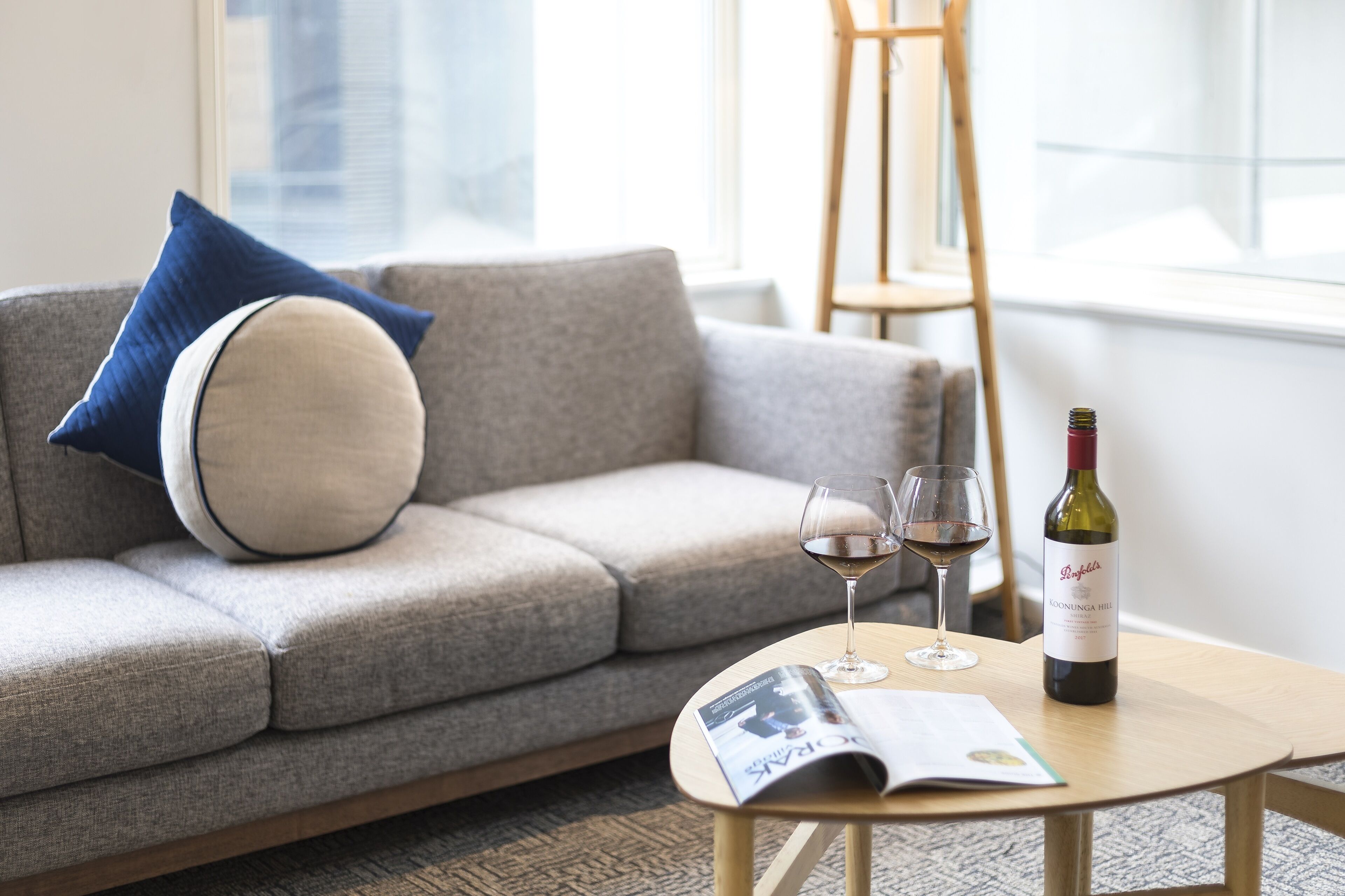 Ein Wohnzimmer mit grauem Sofa, einem Holztisch, einer Weinflasche und zwei Weingläsern.