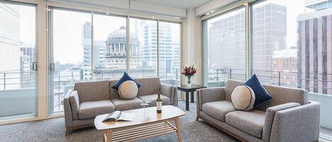 A modern hotel room with two sofas, a coffee table, and large windows offering a city view.