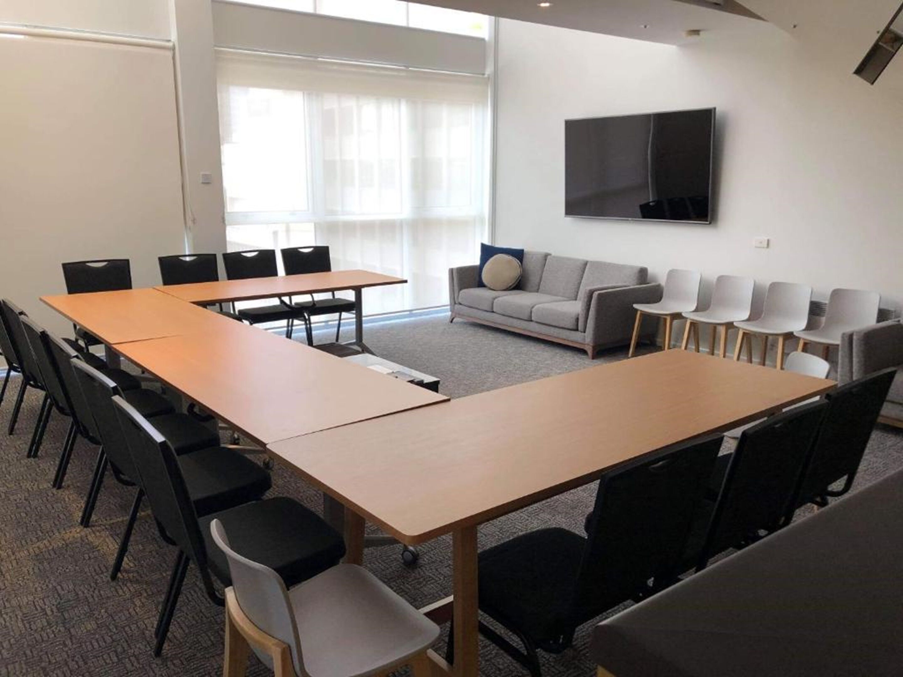 A conference room with a long table, several chairs, a sofa, and a TV on the wall.