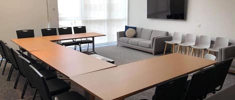 A conference room with a long table, several chairs, a sofa, and a TV on the wall.
