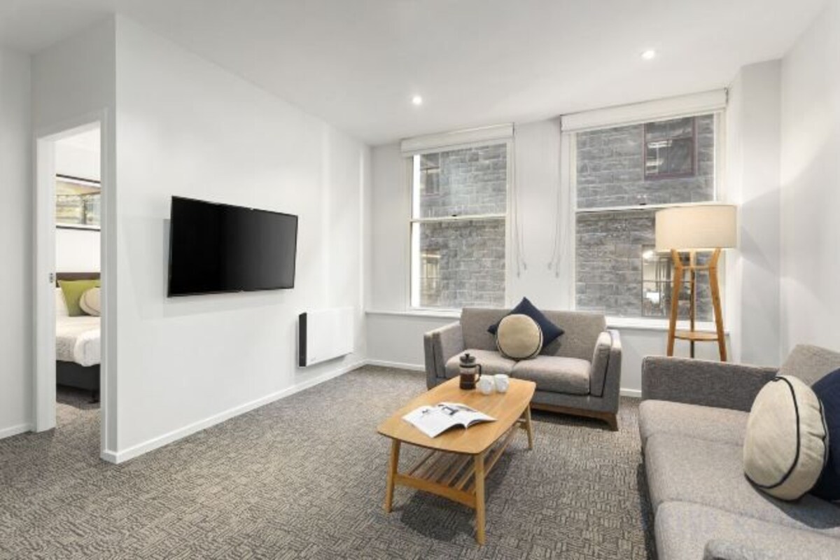 A modern living room with a flat-screen TV, two sofas, a coffee table, and a lamp.