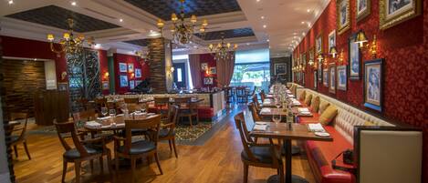 Un restaurante con mesas y sillas de madera, una zona de bar y paredes rojas decoradas con cuadros.