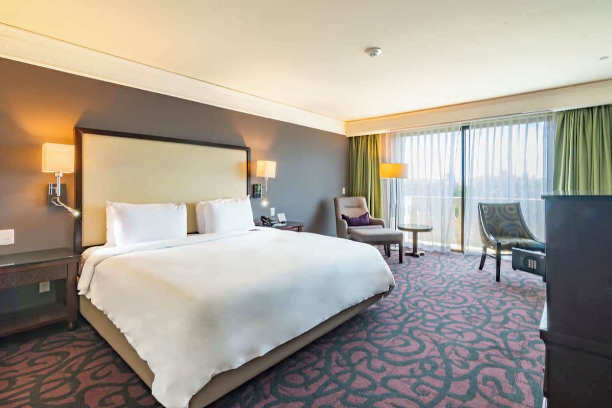 A hotel room with a large bed, a desk, a chair, and a view of the city through the window.