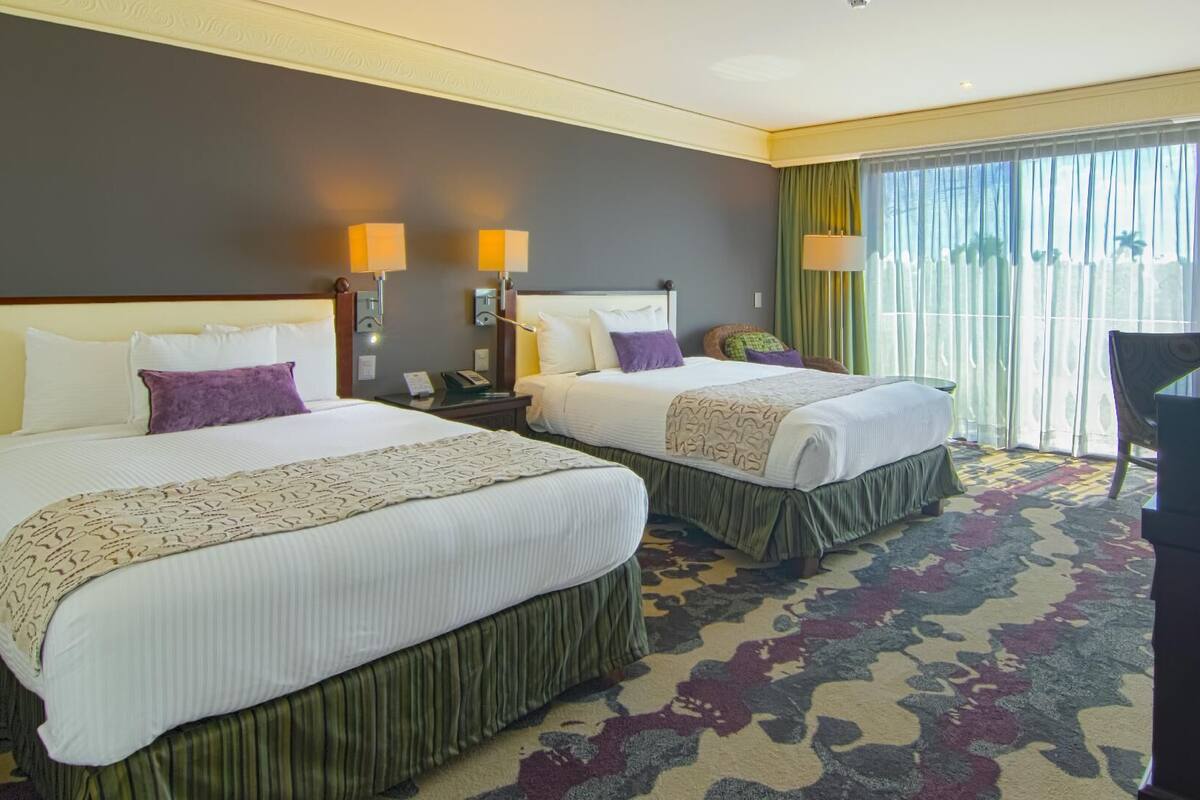 A hotel room with two beds, a desk, a chair, and a large window with curtains.