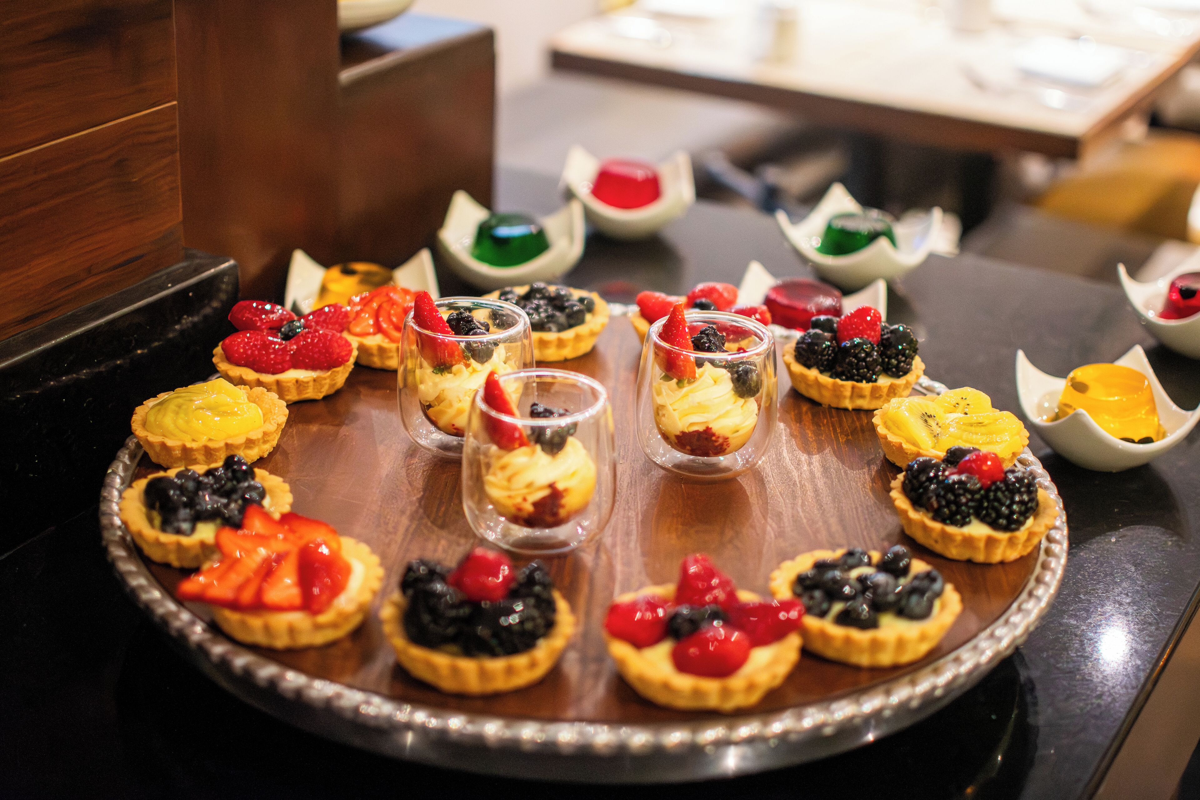 Una bandeja con diversos postres, incluyendo tartas y vasos con fruta.