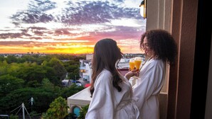 Zwei Personen genießen Getränke auf einem Balkon mit Sonnenuntergang.
