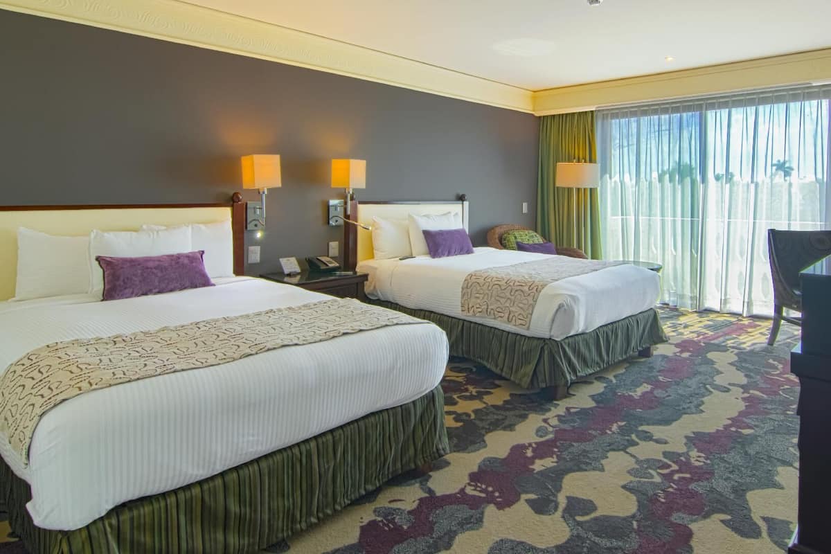 A hotel room with two beds, a desk, a chair, and a large window with curtains.