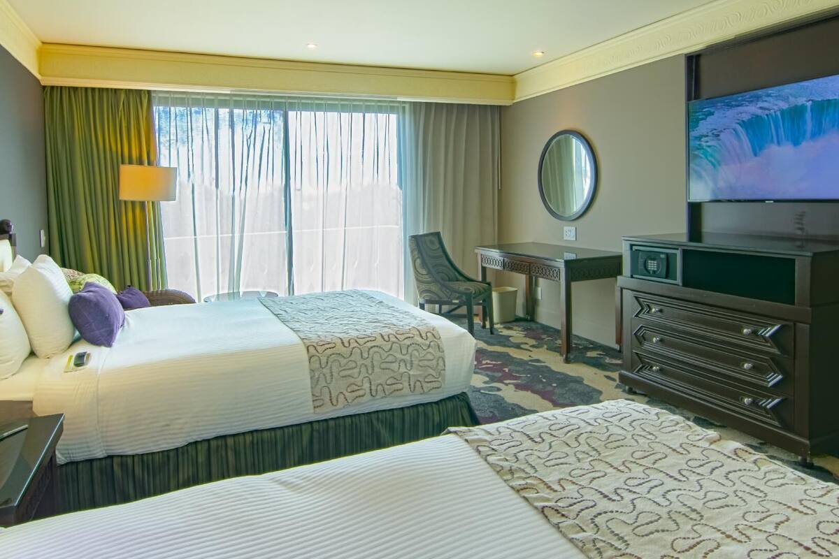 A hotel room with a bed, a desk, a chair, a television, and a dresser.