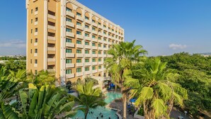 Ein Hotel mit mehreren Etagen, einem Schwimmbad und üppiger Bepflanzung.
