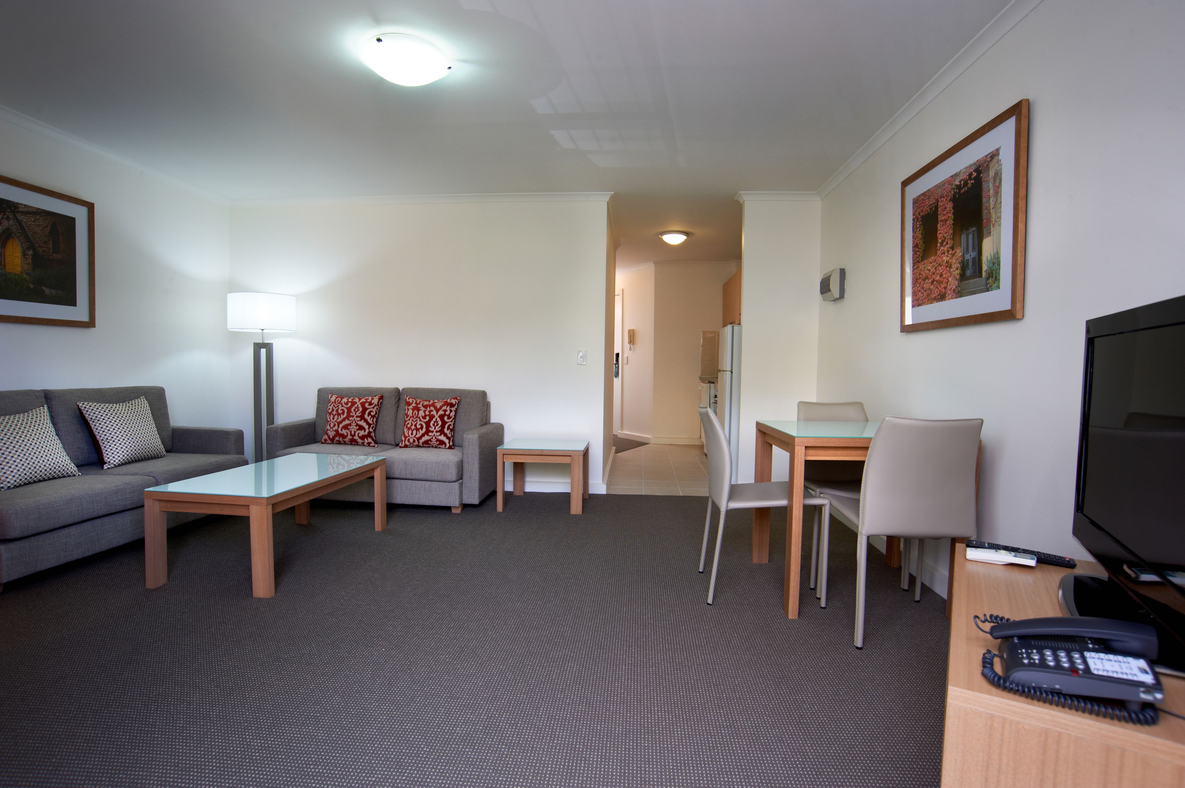 A hotel room with a grey sofa, two armchairs, a coffee table, a dining table with chairs, a TV, and a telephone.