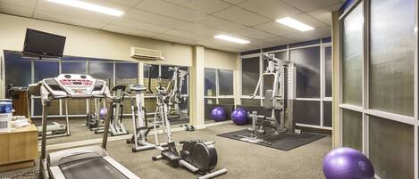 A gym with treadmills, elliptical machines, and exercise balls.