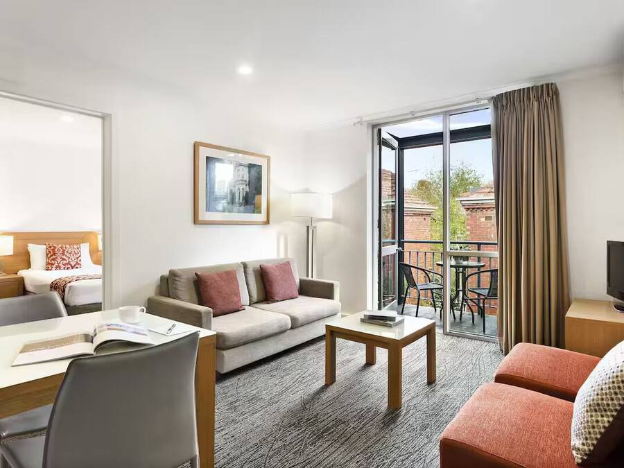 A hotel room with a sofa, a dining table, a TV, and a balcony with a table and chairs.