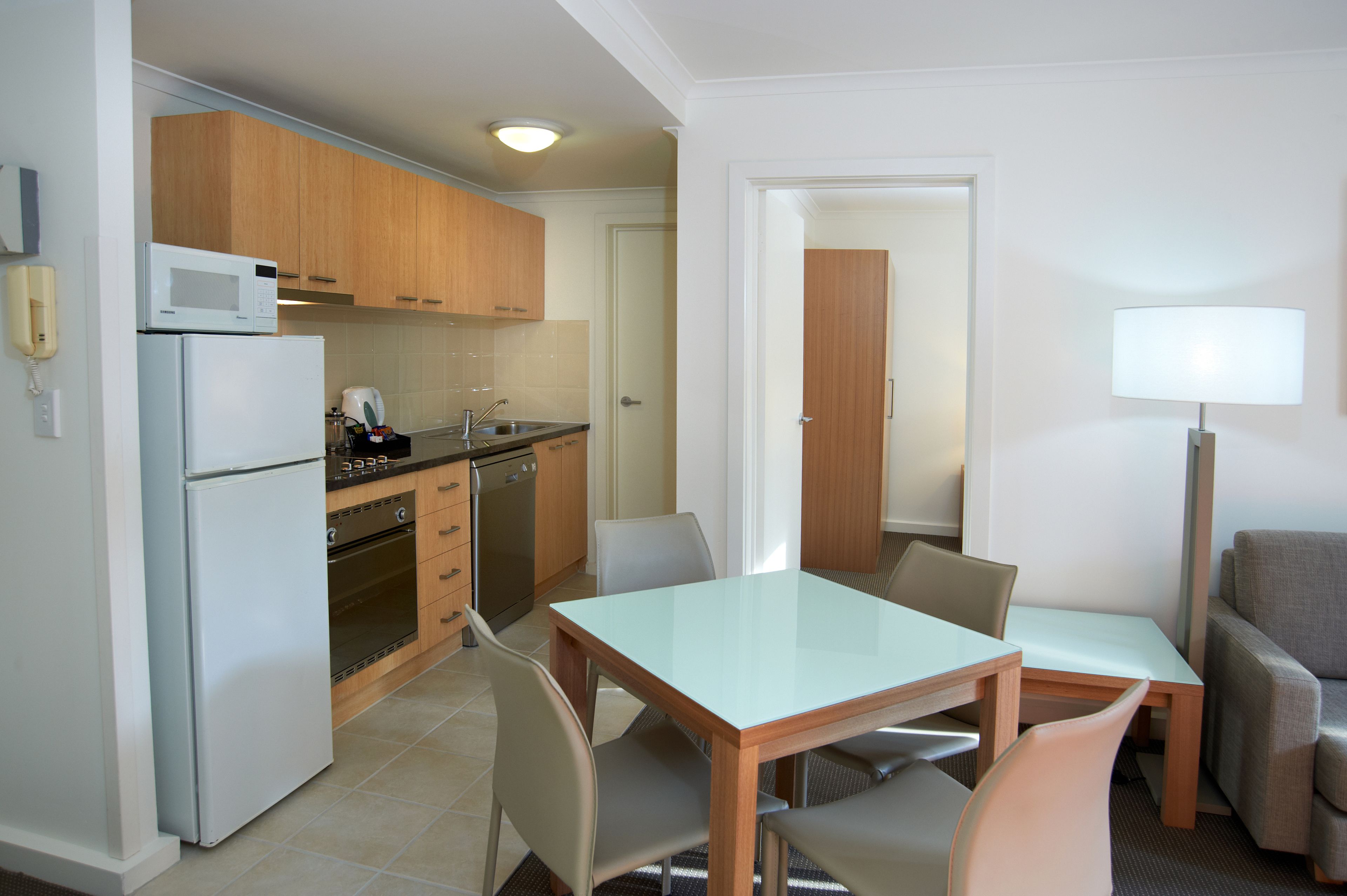 A compact kitchen with a refrigerator, microwave, stove, and sink. There is a dining table with chairs and a sofa in the adjacent living area.