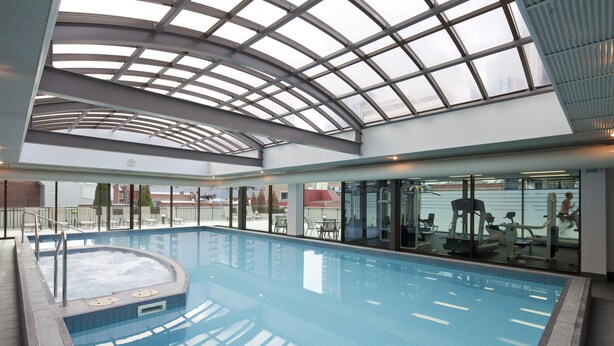 Une piscine intérieure dotée d’un toit en verre, d’une eau cristalline et d’équipements de musculation en arrière-plan.