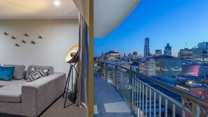 Un balcon avec vue sur la ville, un canapé, une lampe sur pied et un mur orné de motifs géométriques.
