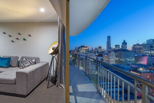 Un balcón con vista a la ciudad, un sofá, una lámpara de pie y una pared con decoraciones geométricas.