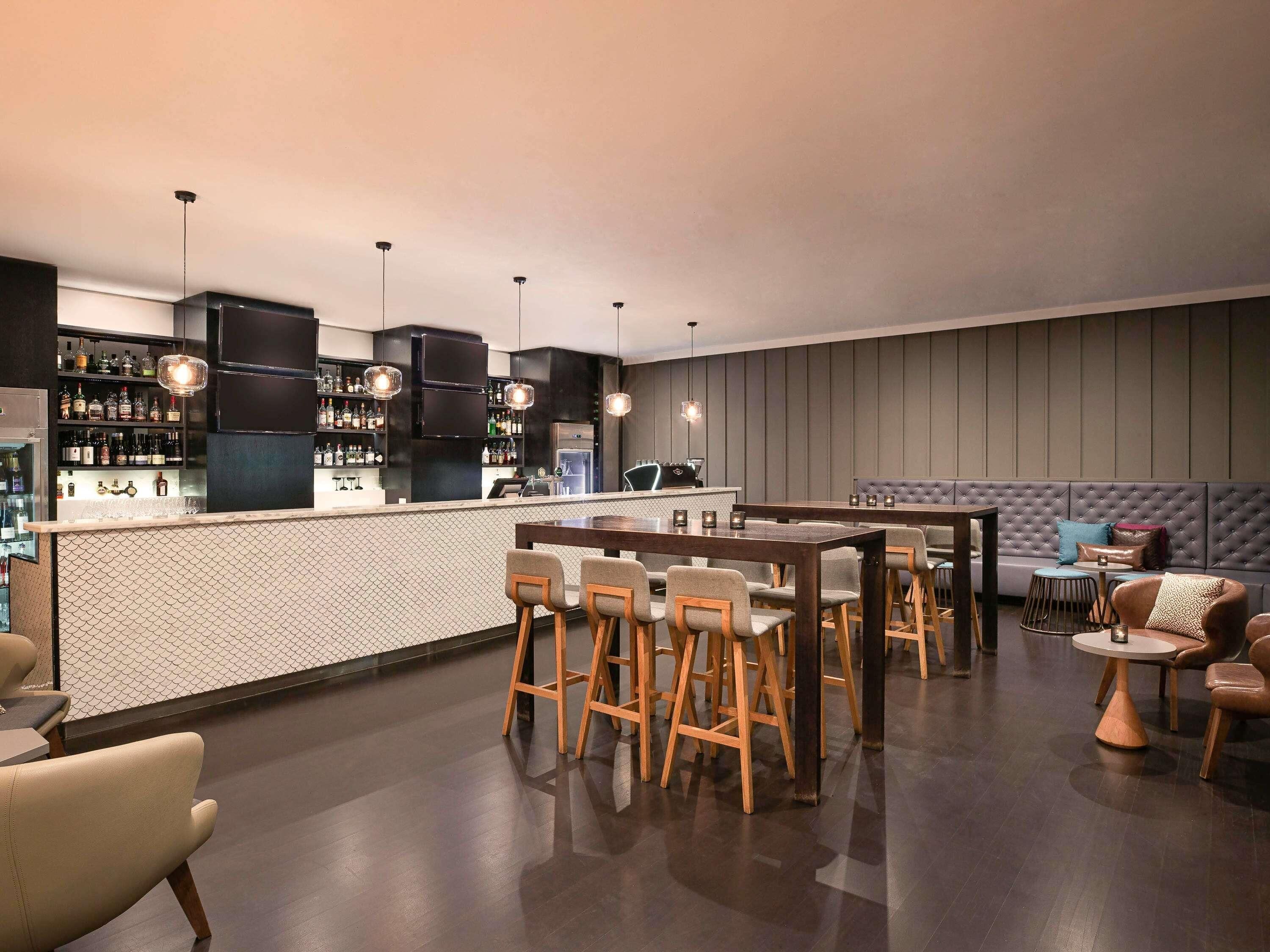 A modern bar area with a counter, stools, and a seating area with a sofa and chairs.