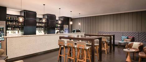 A modern bar area with a counter, stools, and a seating area with a sofa and chairs.