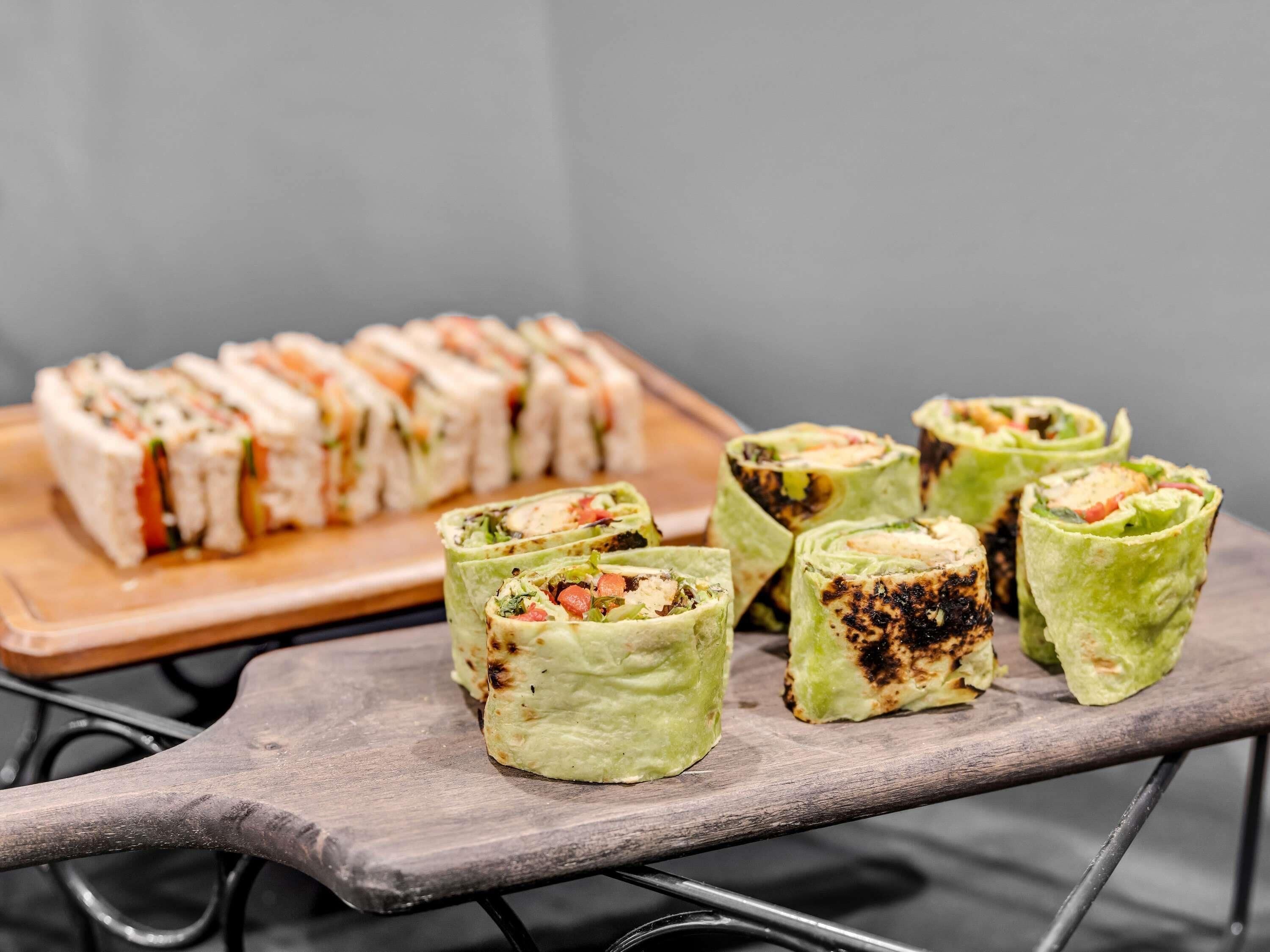 A tray of food items, including wraps and rolls, on a wooden board.