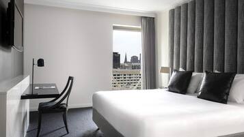 A hotel room with a bed, a desk, a chair, a TV, and a view of the cityscape.