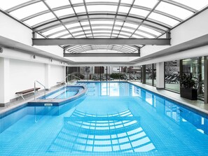 An indoor swimming pool with a glass ceiling, clear blue water, and lounge chairs by the pool. - Mantra on Russell Melbourne (Melbourne)