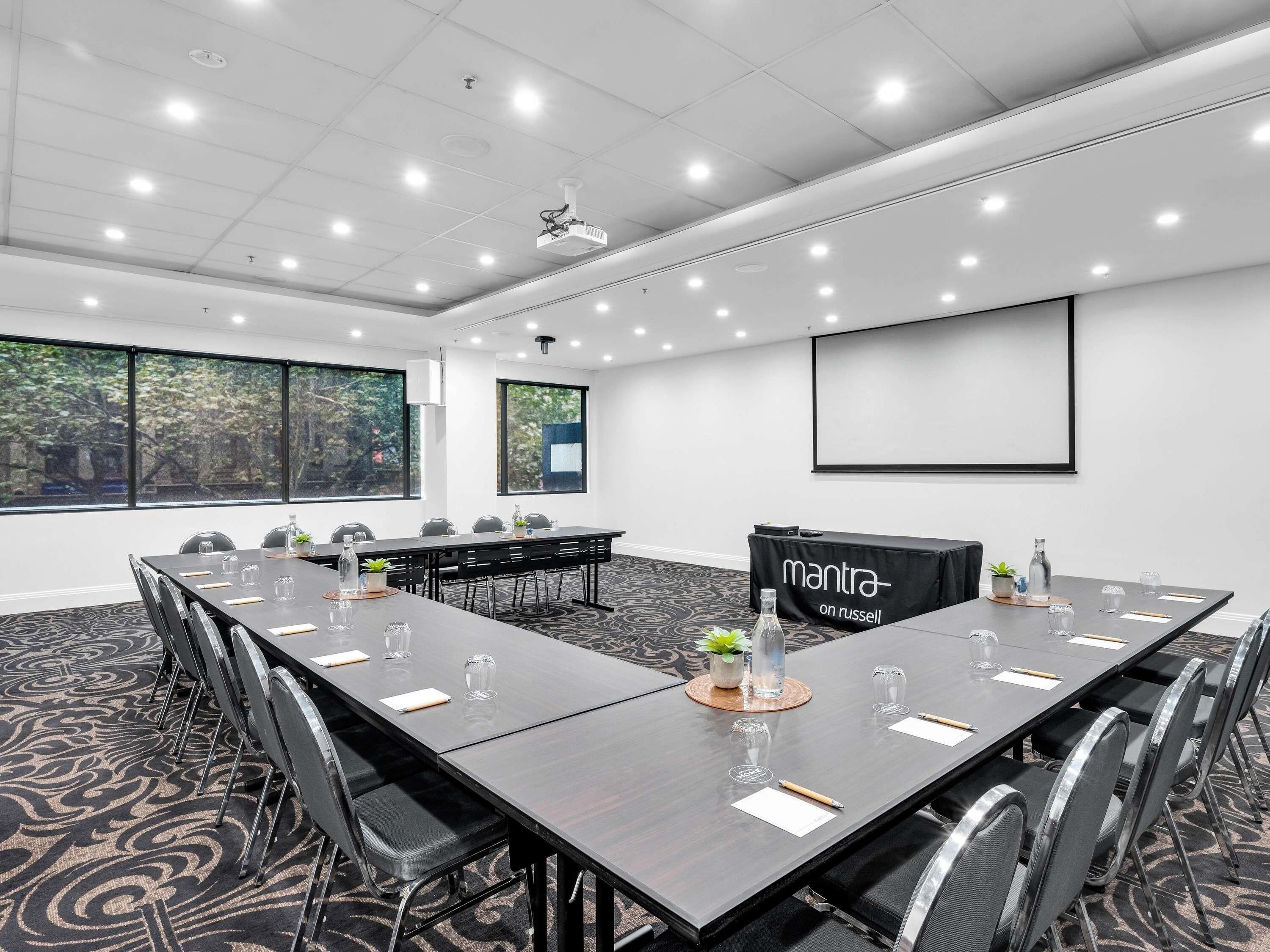 A conference room with a long table, chairs, a projector, and a screen.