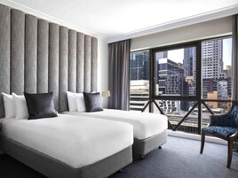 Habitación de hotel con dos camas, un ventanal grande con vista a la ciudad, una silla y una lámpara.