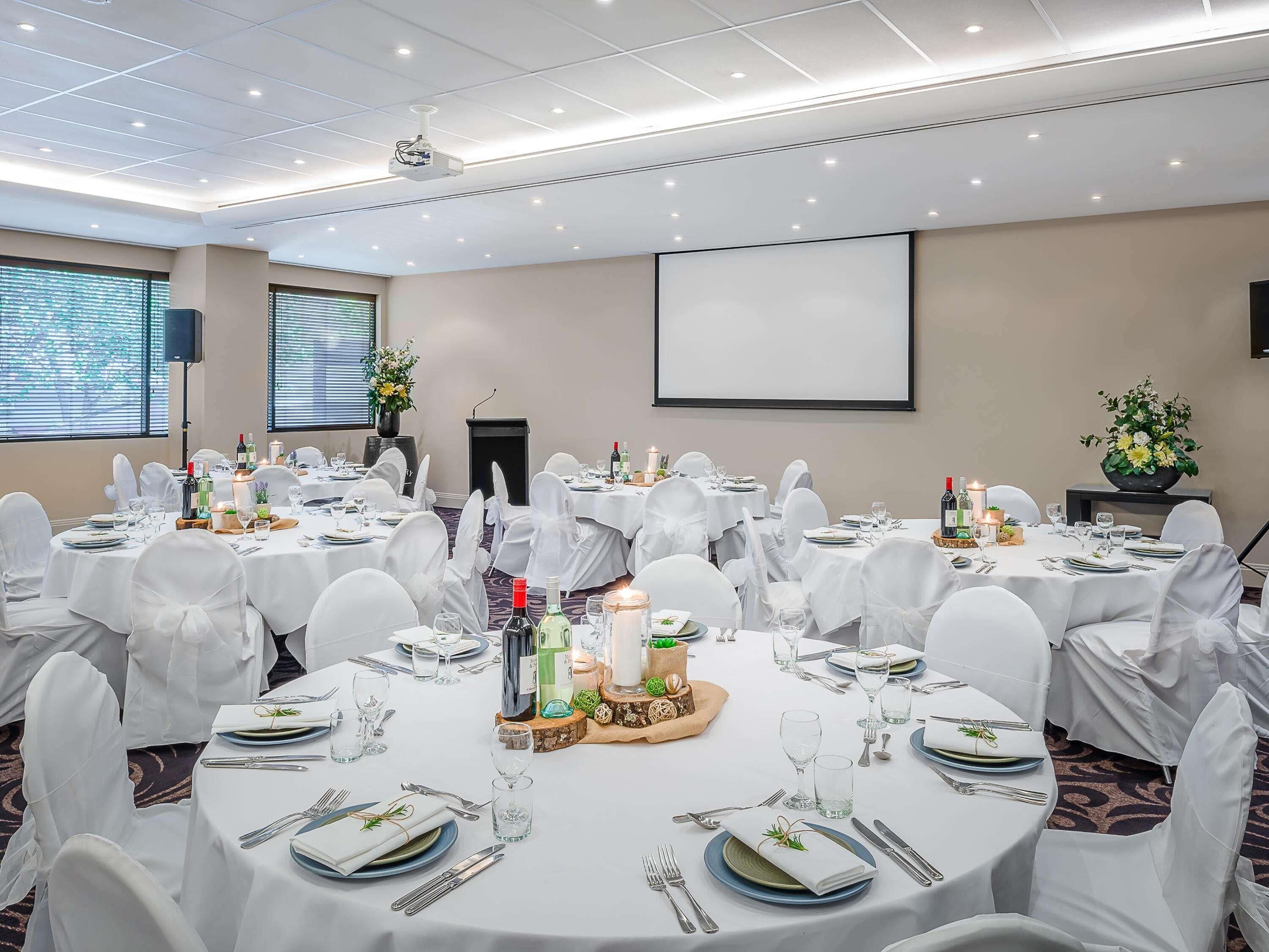 A conference room with round tables, white chairs, and a projector screen.