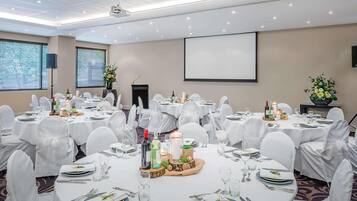 A conference room with round tables, white chairs, and a projector screen.