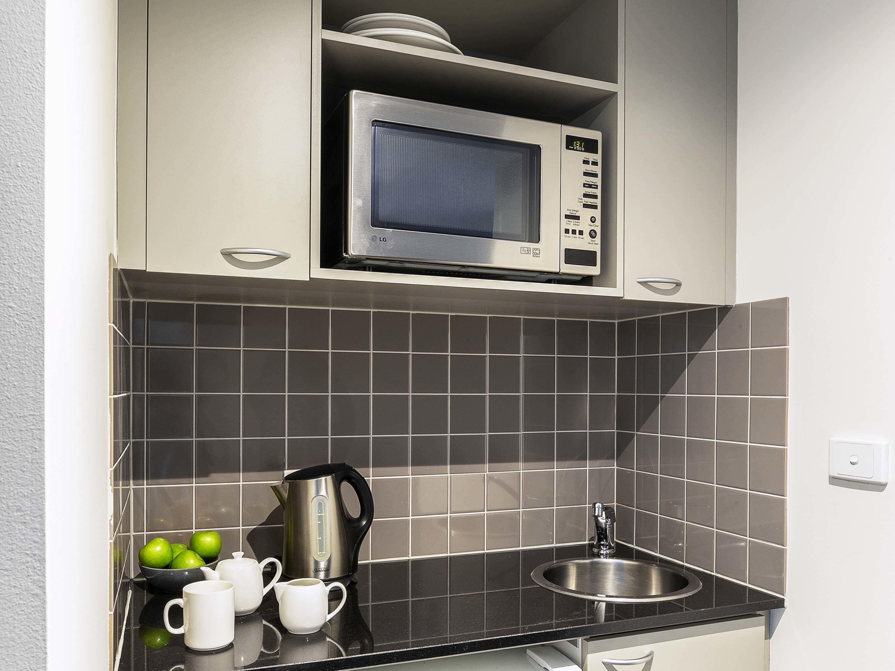 Een kleine keuken met een magnetron, waterkoker, wastafel en een klein aanrecht.