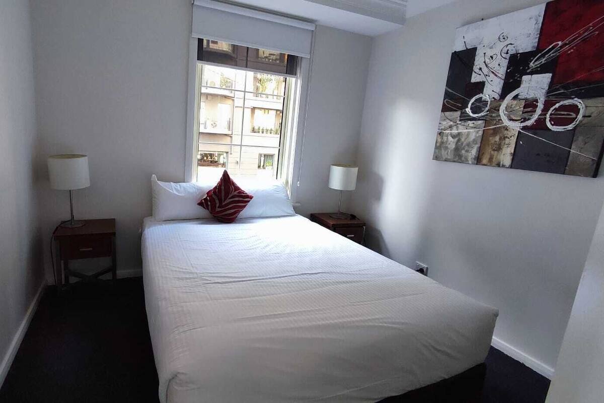 A small, neatly arranged bedroom with a single bed, two bedside tables, and a window providing natural light.