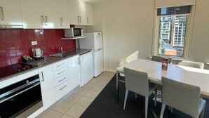 Eine kleine Küche mit weißen Schränken, einer roten Spritzschutzwand, einer Mikrowelle, einem Kühlschrank und einem Essbereich mit Tisch und Stühlen.