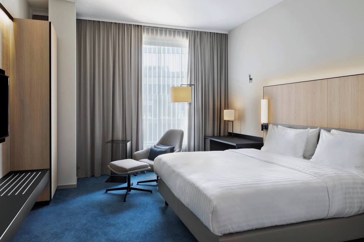 Une chambre d’hôtel avec un grand lit, un bureau, une chaise, une télévision et une fenêtre avec des rideaux.