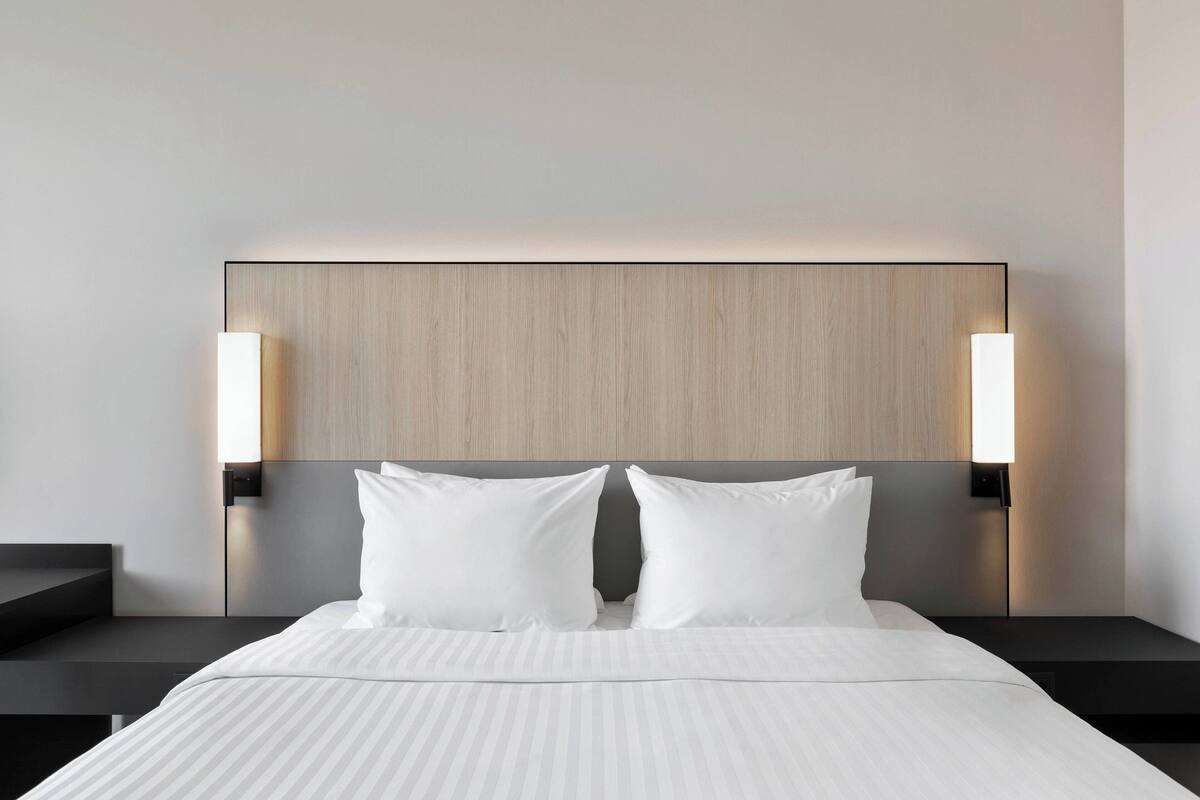 Une chambre d’hôtel moderne avec un grand lit, deux tables de chevet et des lampes fixées au mur.