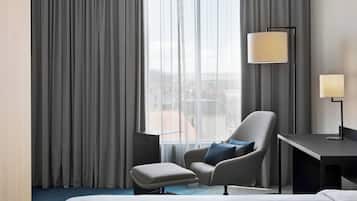 A hotel room with a bed, a chair, a desk, and a lamp.