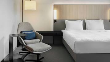 A modern hotel room with a bed, a desk, a chair, and a lamp.