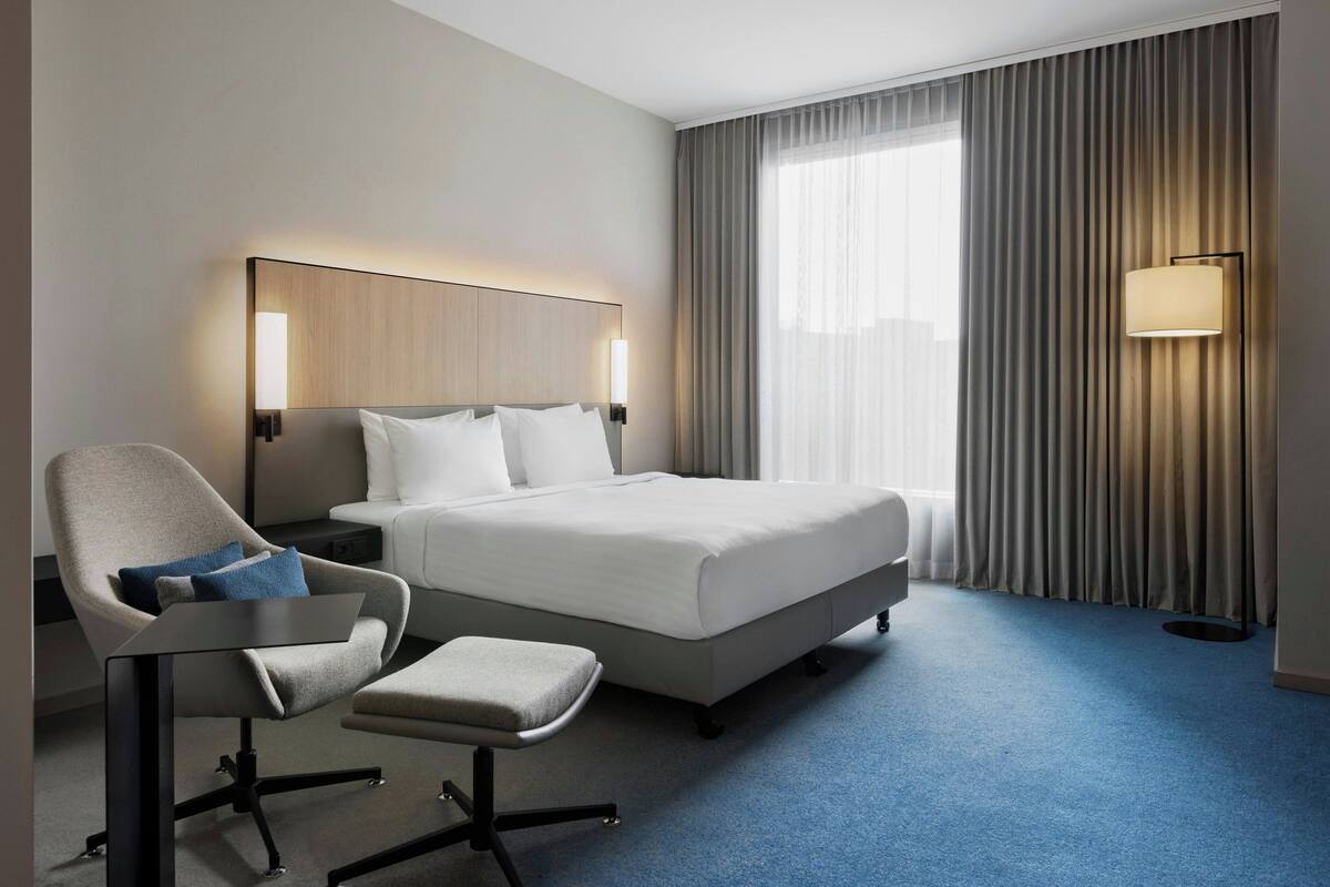 Une chambre d’hôtel avec un lit, une chaise, un bureau et une lampe.